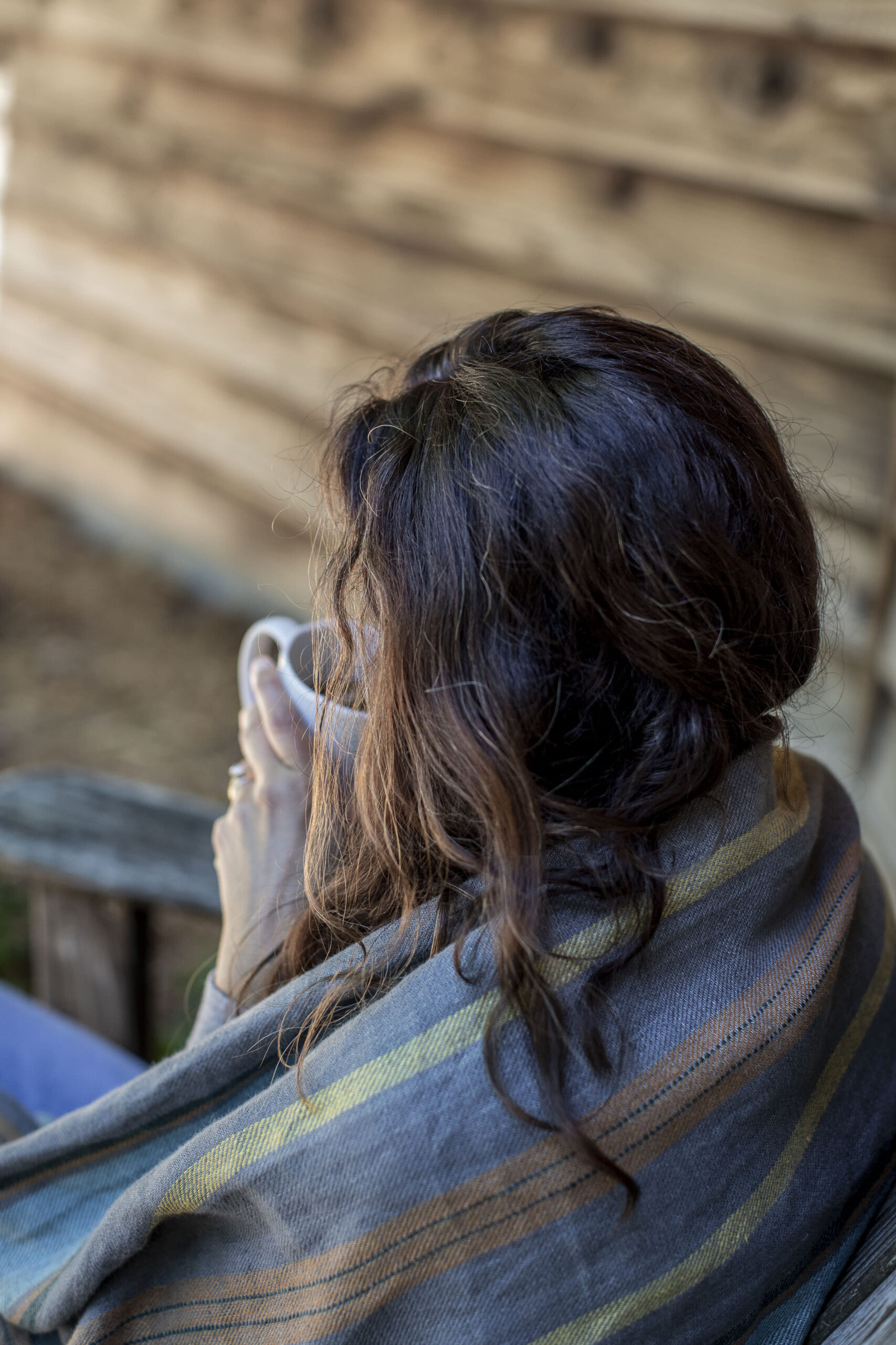 A woman sitting outdoors wrapped in a blanket, holding a cup of coffee during a quiet moment of healing after divorce